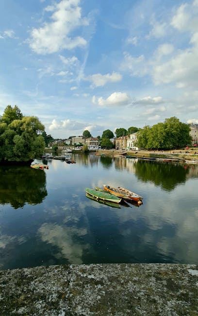 An aerial view of Kingston's riverside, taken during the golden hour, showcasing a gently flowing river bordered by lush trees and well-maintained garden beds. In the background, a variety of resident
